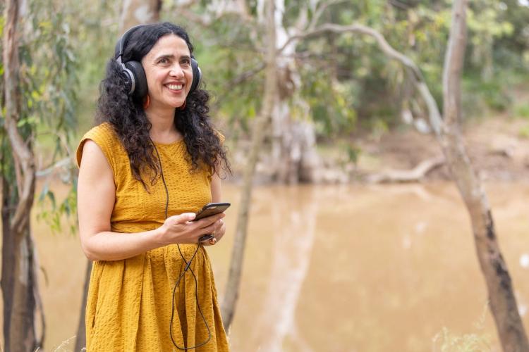 River Whispers - person with headphones and holding a mobile phone